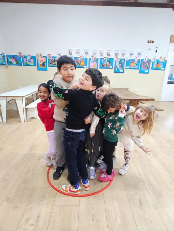 A group of children laughing together piled inside a hula hoop during indoor play