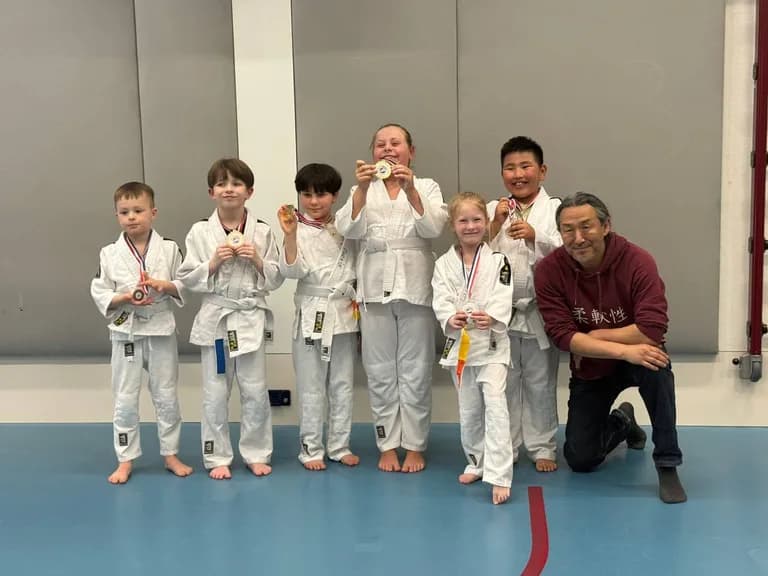 A judo team of students proudly holding medals with their coach