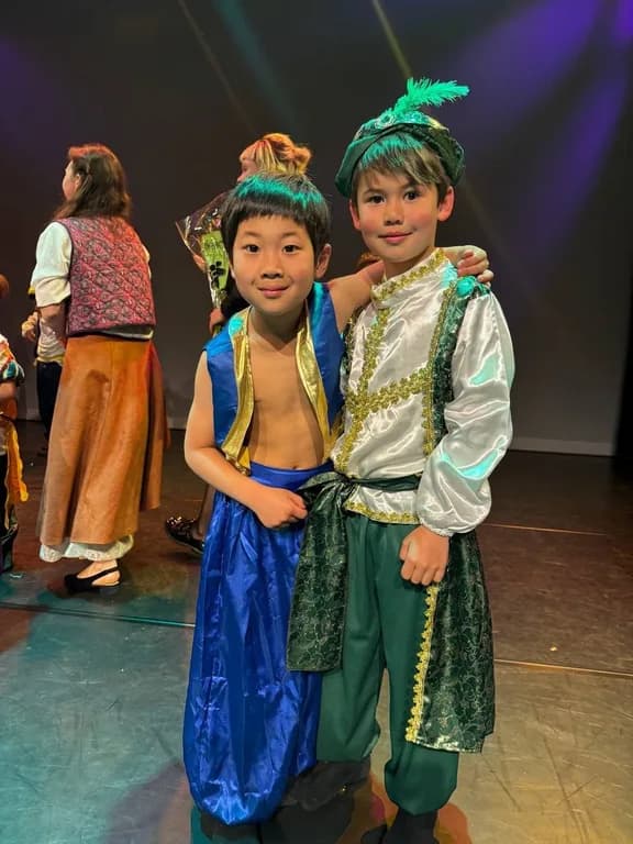 Two TISA students in elaborate theatre costumes smiling on stage